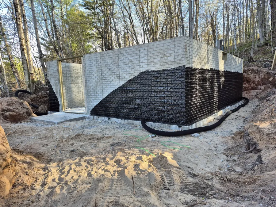 Foundation walls coated black below grade, with drain tile laid around the base before backfill