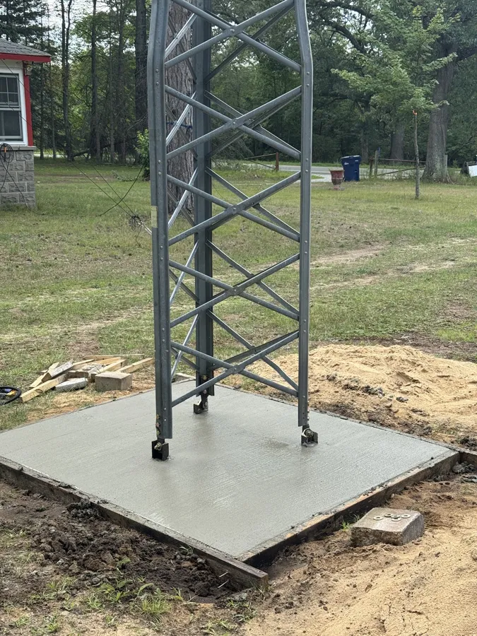 Steel lattice tower standing on its finished concrete pad, a house in the background