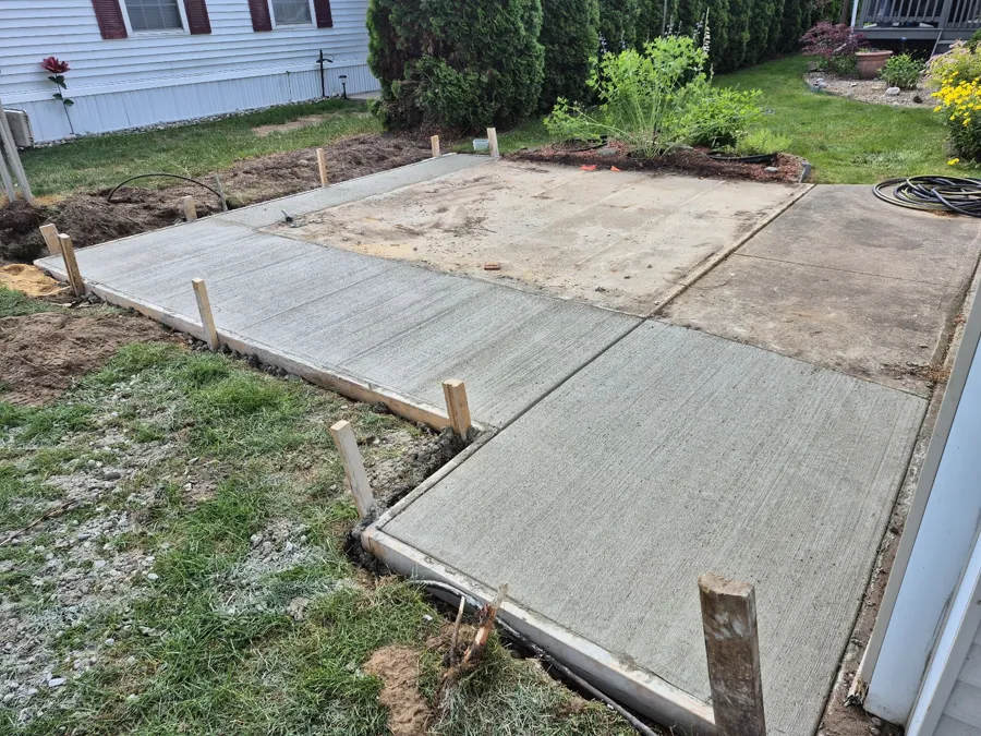 L-shaped concrete walkway and pad poured beside a house, stakes and forms still in place