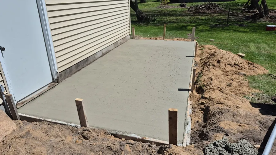 Broom-finished concrete slab poured against the side of a building, forms still staked